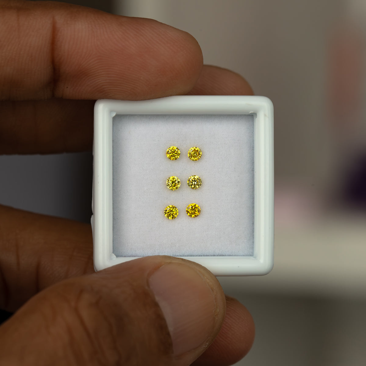 Small tray of three yellow diamond pairs held between fingers for scale.