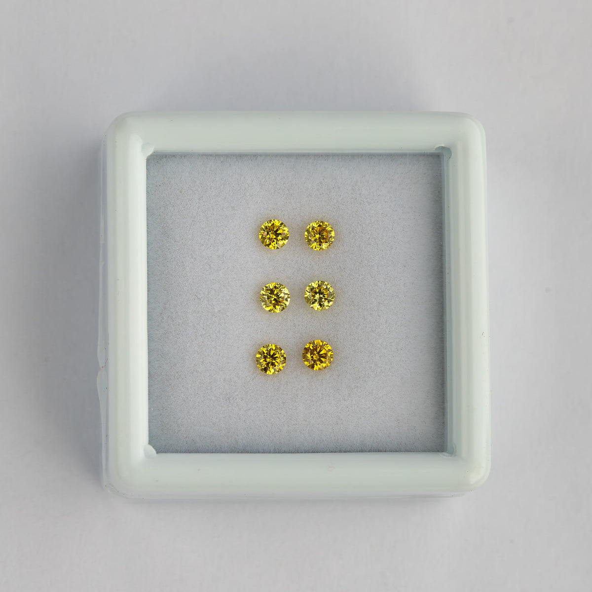 Wide view of the three yellow diamond pairs in a white tray on a pale surface.