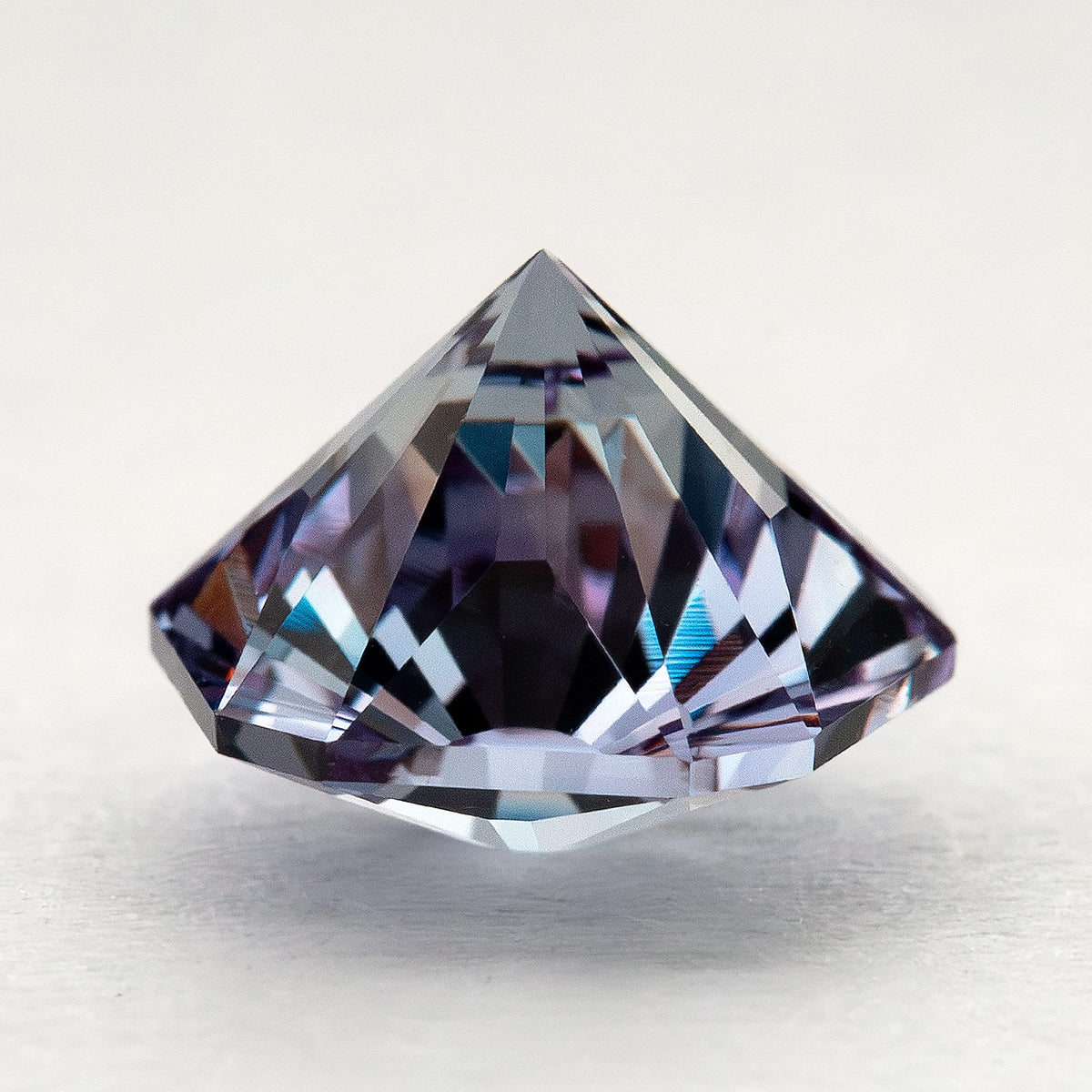 Pointed pavilion and side facets of the pentagon lab-grown sapphire resting on a pale surface.