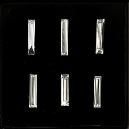 Six long baguette diamonds arranged in two rows of three on black backing, showing their different lengths, widths and step-facet reflections; sold individually by selection.