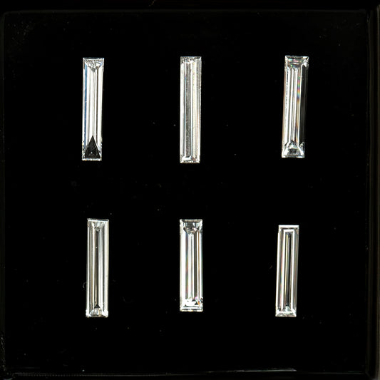 Six long baguette diamonds arranged in two rows of three on black backing, showing their different lengths, widths and step-facet reflections; sold individually by selection.
