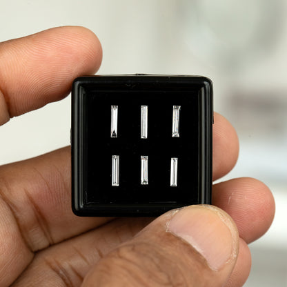 Wider fingertip view of the black box containing six individually selectable baguette diamonds, showing the box size and surrounding hand.