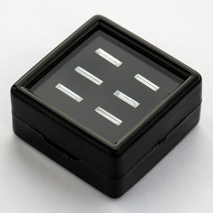 Low angled view of the black baguette-diamond display box on a pale surface, showing the tray depth and reflected faces of the six choices.