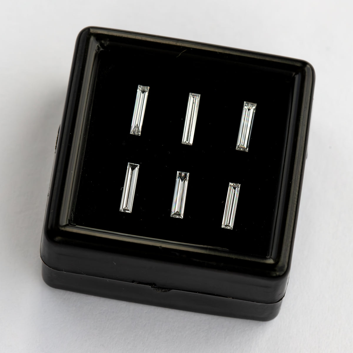 Black box of six long baguette diamond options viewed diagonally from the front, with light and dark step-facet bands.