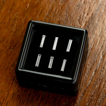 Six baguette diamond choices in a black display box on wood, with a slightly tilted layout and varying reflected brightness.