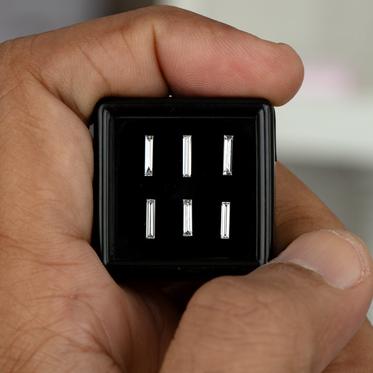 Centered hand-held view of the black baguette selection box, showing all six individual diamond choices against the hand.
