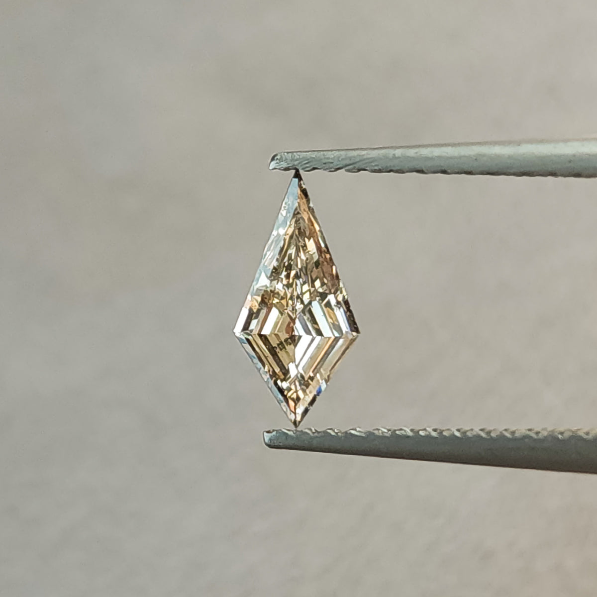 Face-up close view of the exact 0.39 carat elongated kite lab-grown diamond between tweezers, with a pale champagne appearance and angular step-cut reflections.