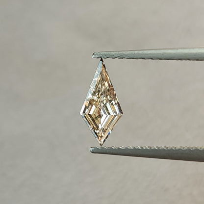Face-up close view of the exact 0.39 carat elongated kite lab-grown diamond between tweezers, with a pale champagne appearance and angular step-cut reflections.