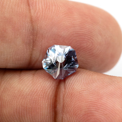 Hanami-cut sapphire between fingertips at an angle, showing white flashes and darker blue-gray facets.