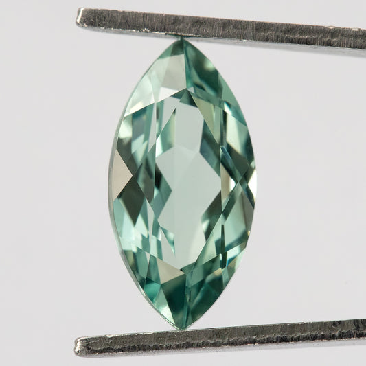 Mint-green marquise lab-grown sapphire held face-up in tweezers on white, showing the pointed outline and central facet pattern.