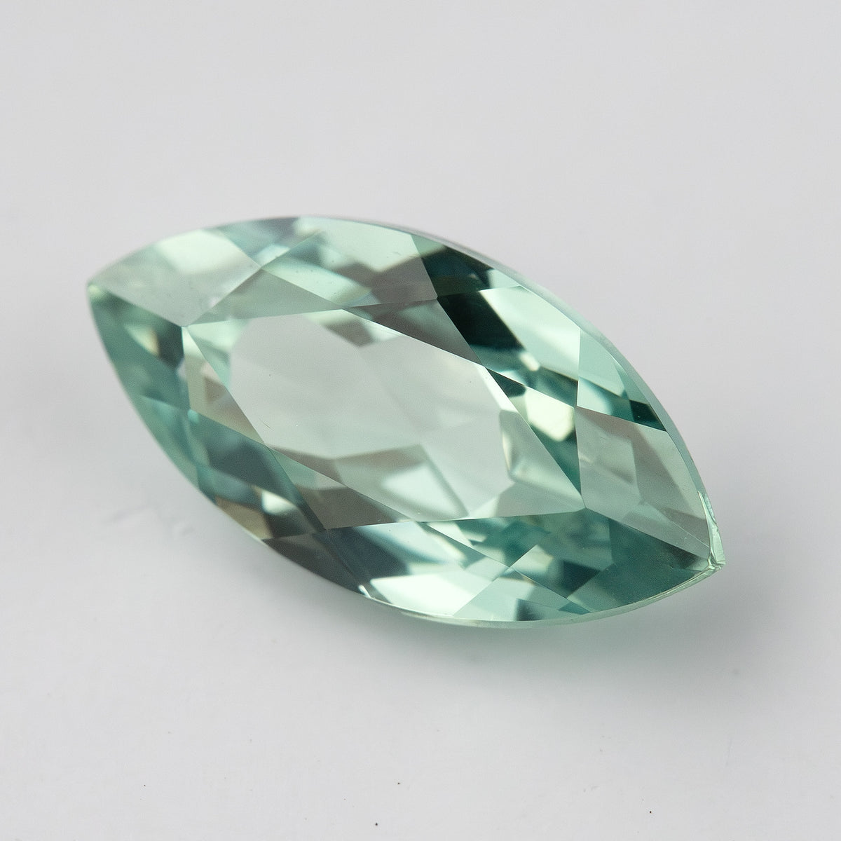 Angled view of a mint-green marquise lab-grown sapphire on a pale background, showing its raised profile and facets.