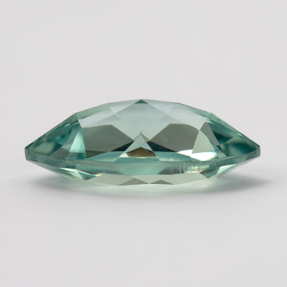 Low side view of a mint-green marquise lab-grown sapphire, showing its faceted profile above a pale surface.