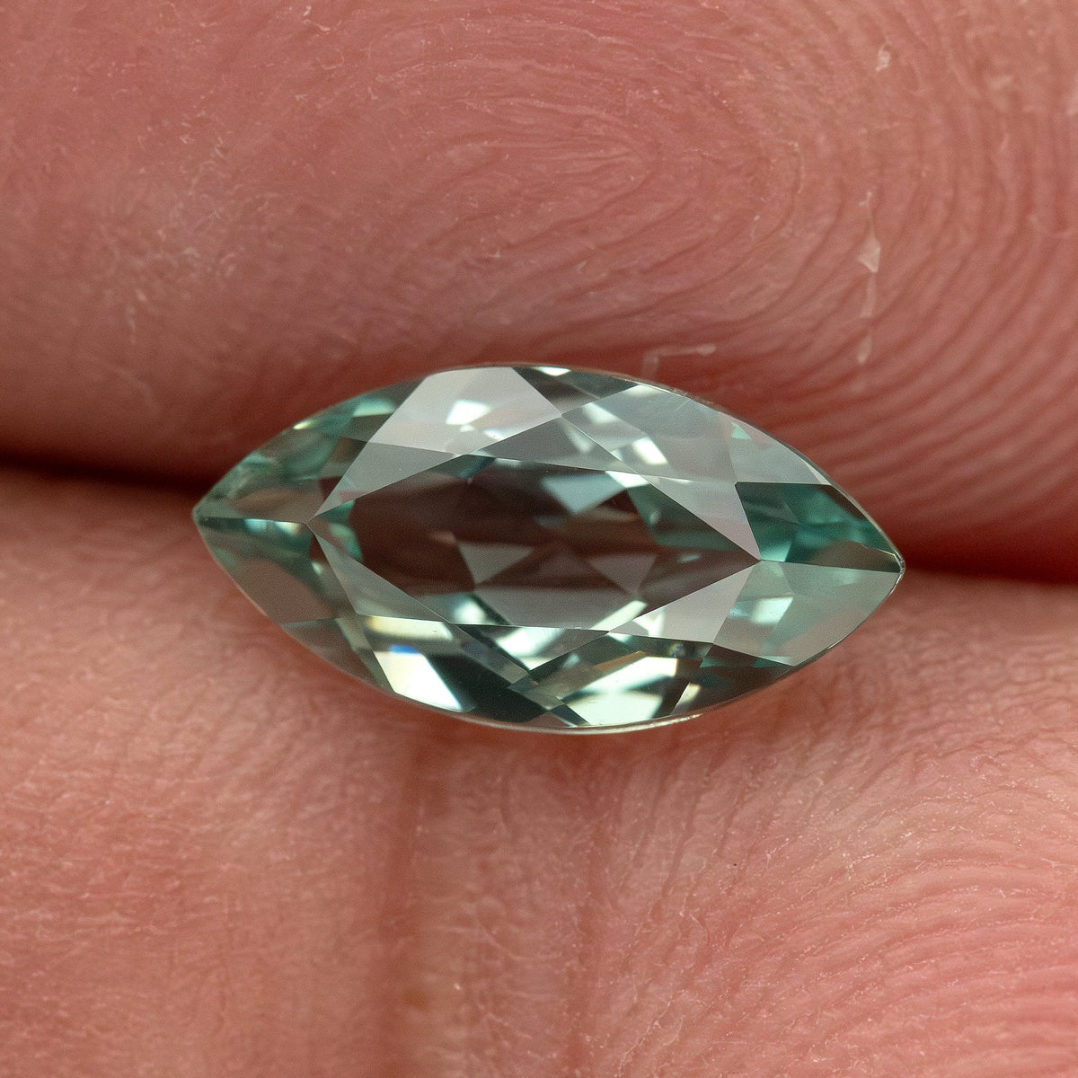 Mint-green marquise lab-grown sapphire resting horizontally against fingers, showing its pointed outline and reflections.