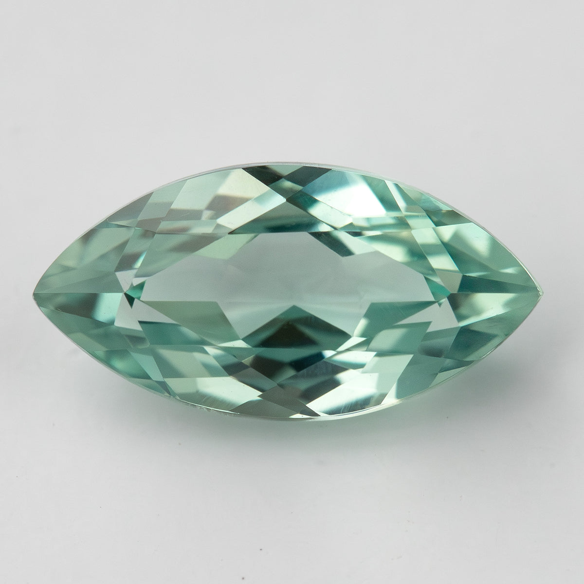 Near face-up view of a mint-green marquise lab-grown sapphire on a pale surface, with bright central facet reflections.