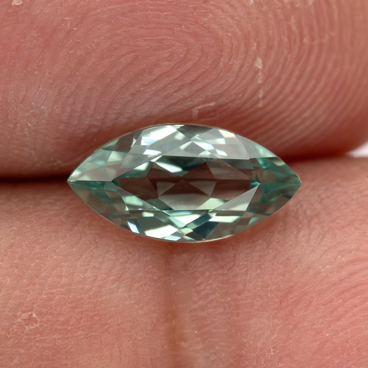 Close view of a mint-green marquise lab-grown sapphire against fingers, showing pale and darker green facet reflections.