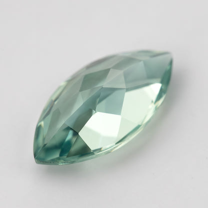 Diagonal view of a mint-green marquise lab-grown sapphire on a pale background, showing its curved sides and pointed ends.