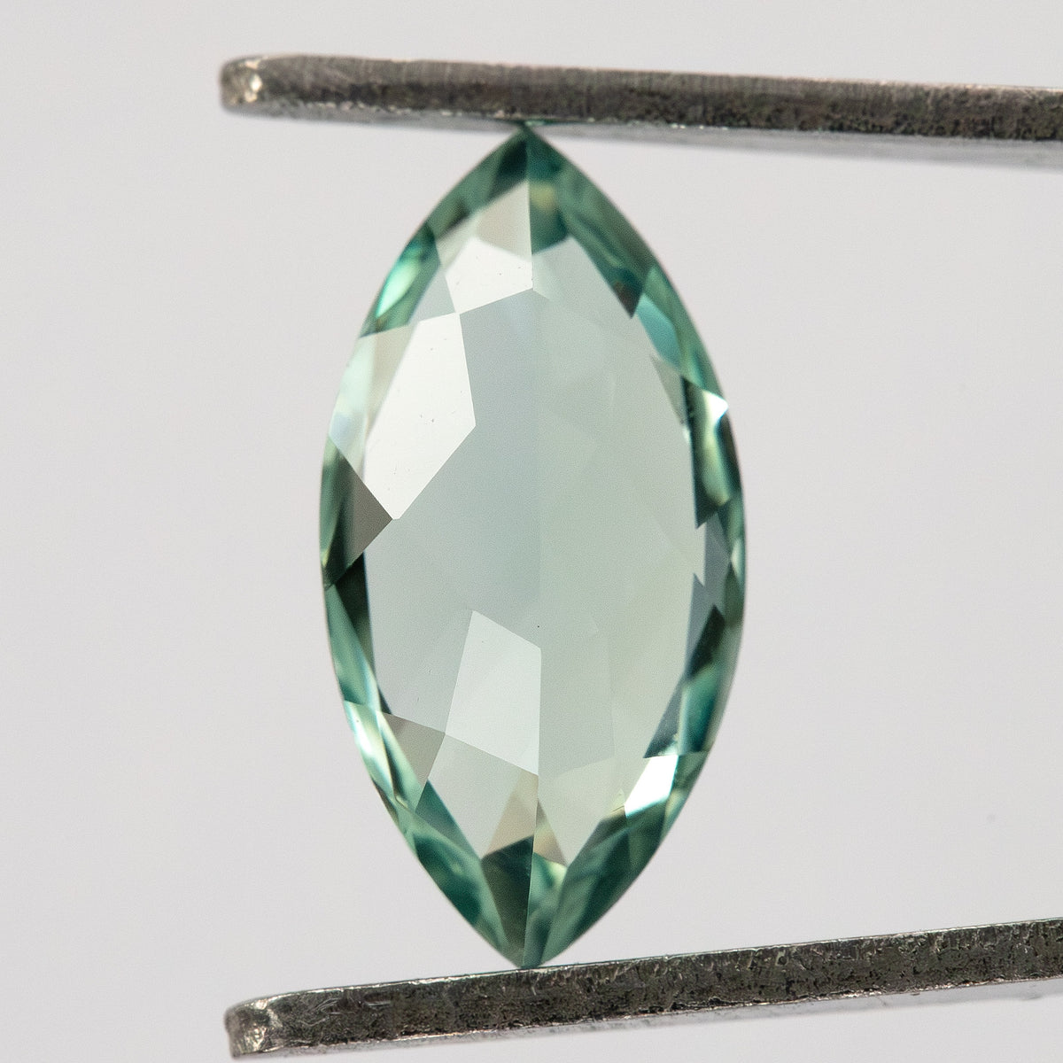 Mint-green marquise lab-grown sapphire between tweezers, with a broad pale central area and green edges.