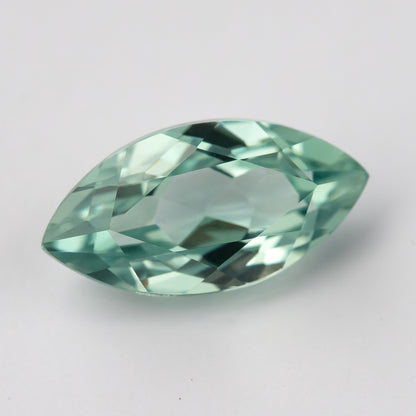 Tilted view of a mint-green marquise lab-grown sapphire on a pale surface, showing green facet reflections.