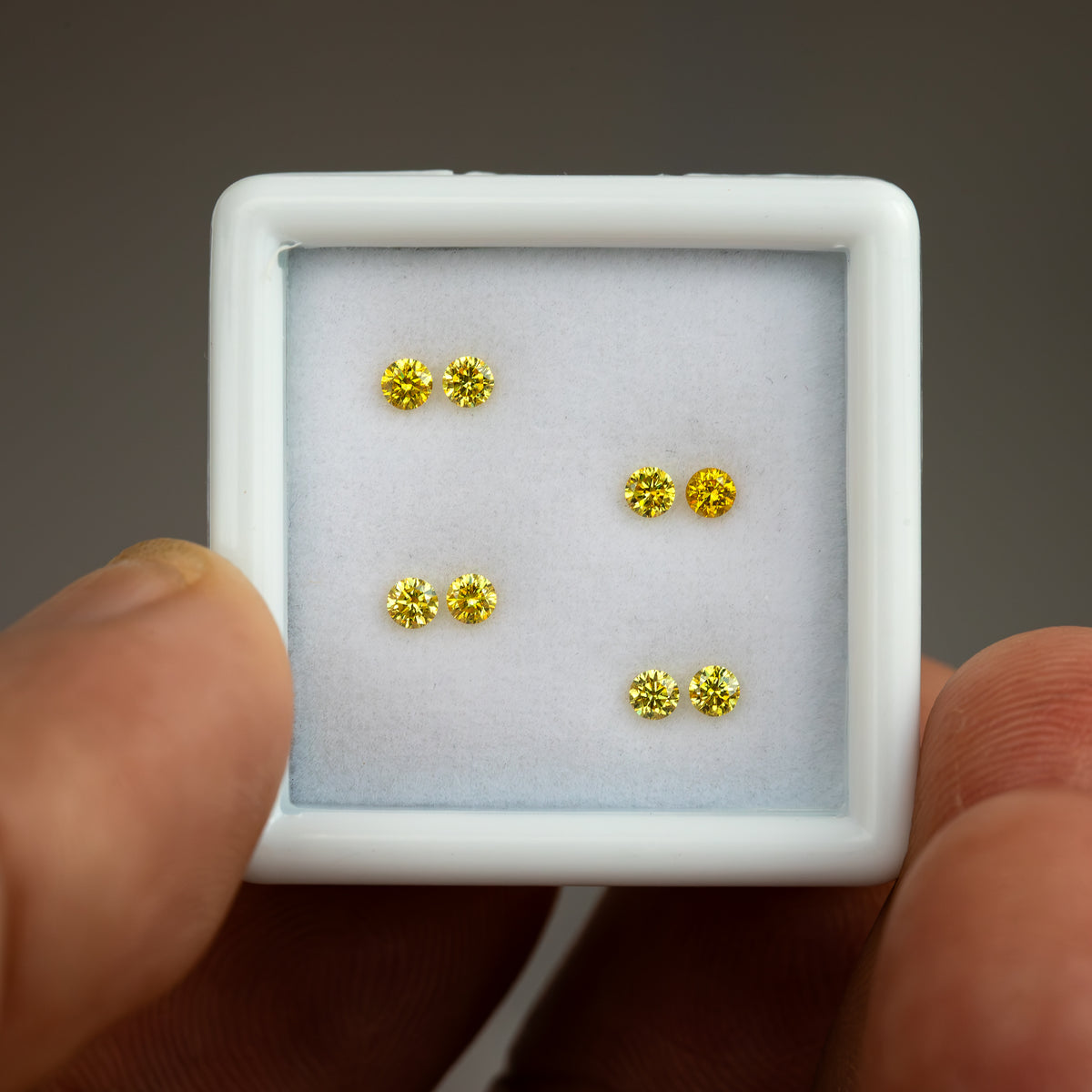 White tray of four yellow diamond pairs held at a slight angle by fingers.