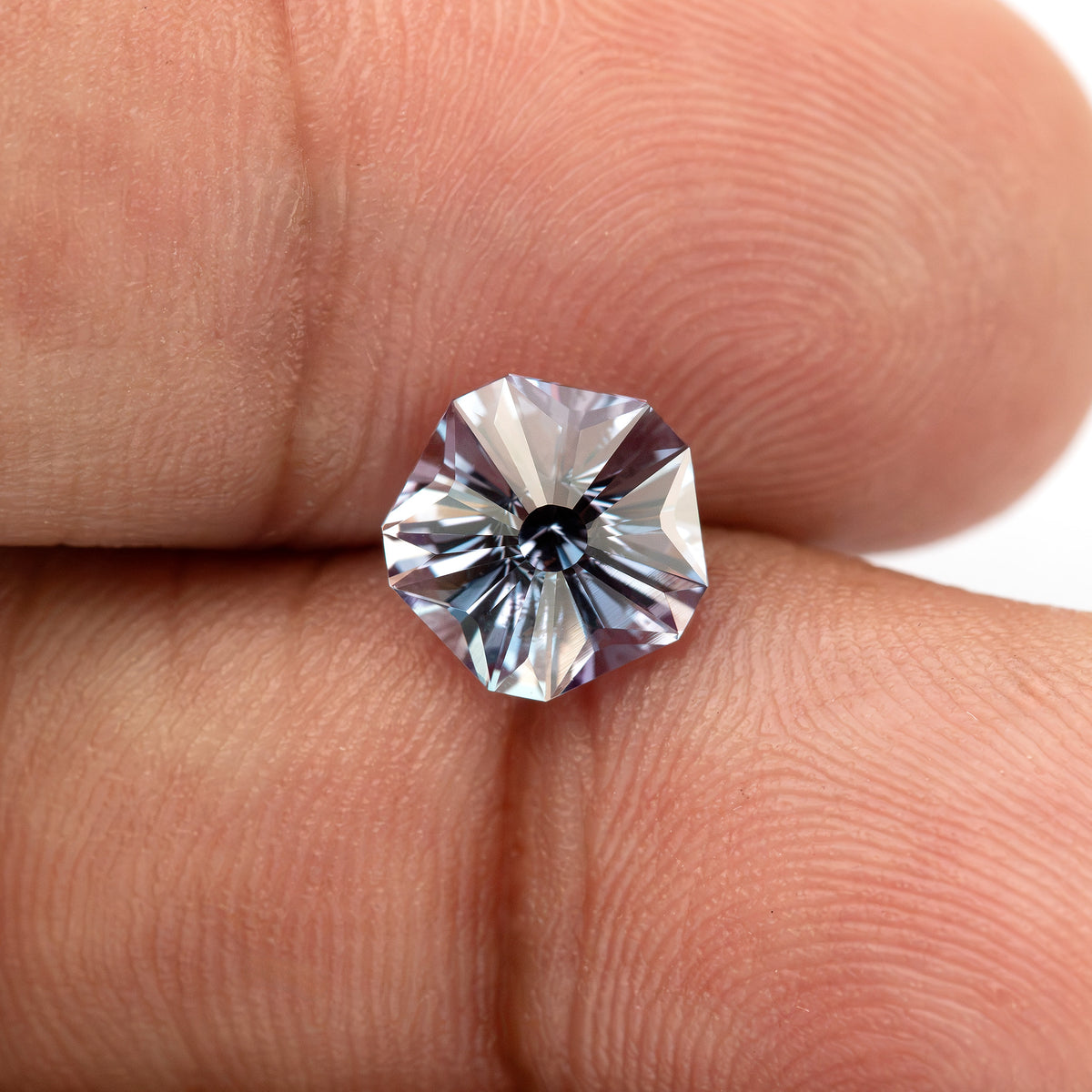 Small face-up pentagon sapphire on a fingertip, showing a bright radial Hanami pattern and surrounding skin for scale.