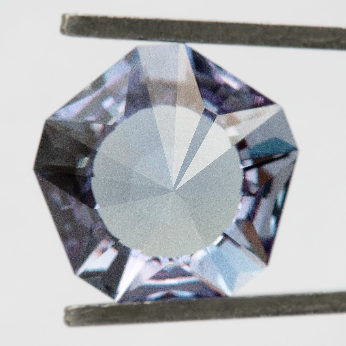 Pavilion-facing view of the lab-grown sapphire held in tweezers, showing a broad central reverse facet.