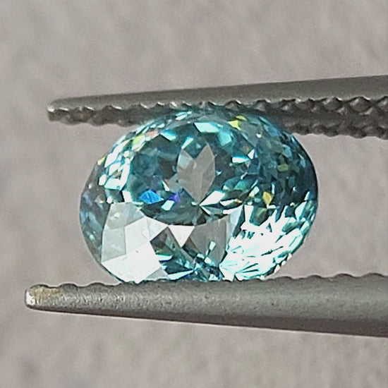 Blue round diamond shown in tweezers, on fingers, on the palm and on a white pad from changing angles.