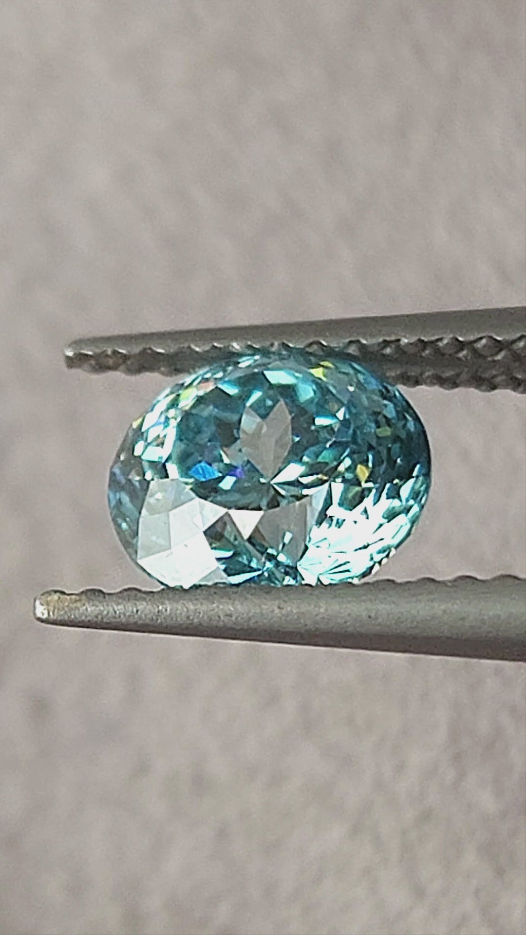 Blue round diamond shown in tweezers, on fingers, on the palm and on a white pad from changing angles.