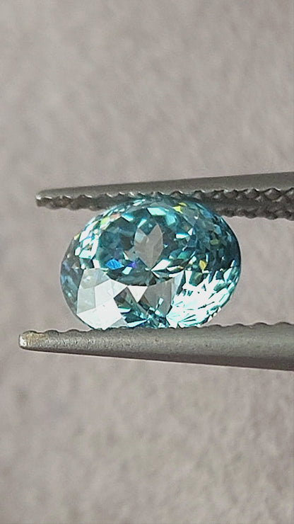 Blue round diamond shown in tweezers, on fingers, on the palm and on a white pad from changing angles.