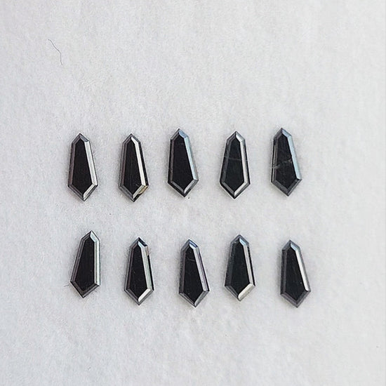 Calibrated black shield diamonds shown in a group, with single-stone tweezers and fingertip views; sold per piece.