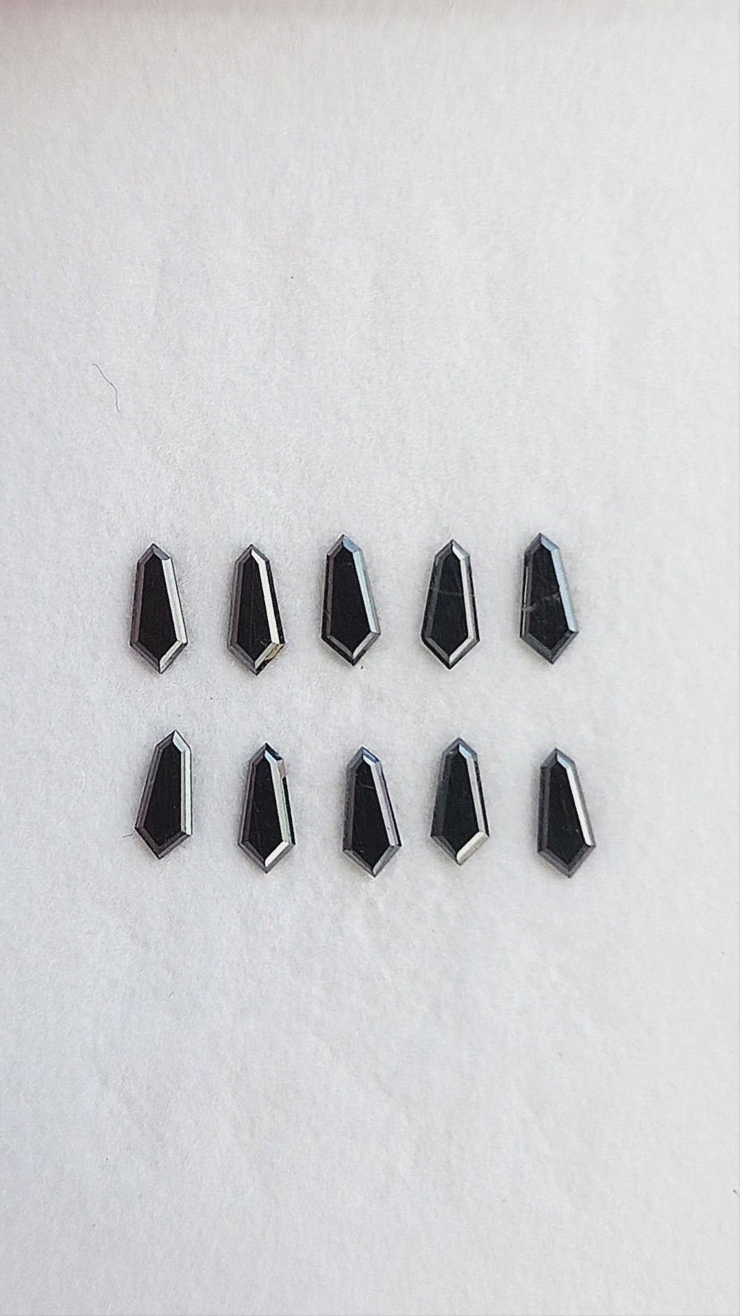 Calibrated black shield diamonds shown in a group, with single-stone tweezers and fingertip views; sold per piece.
