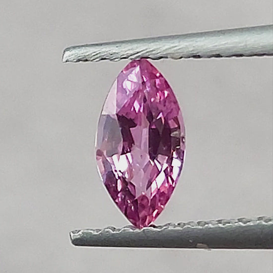 Pink marquise sapphire rotating in tweezers, shown between fingertips, on a cream pad, on a white pad and on a palm.