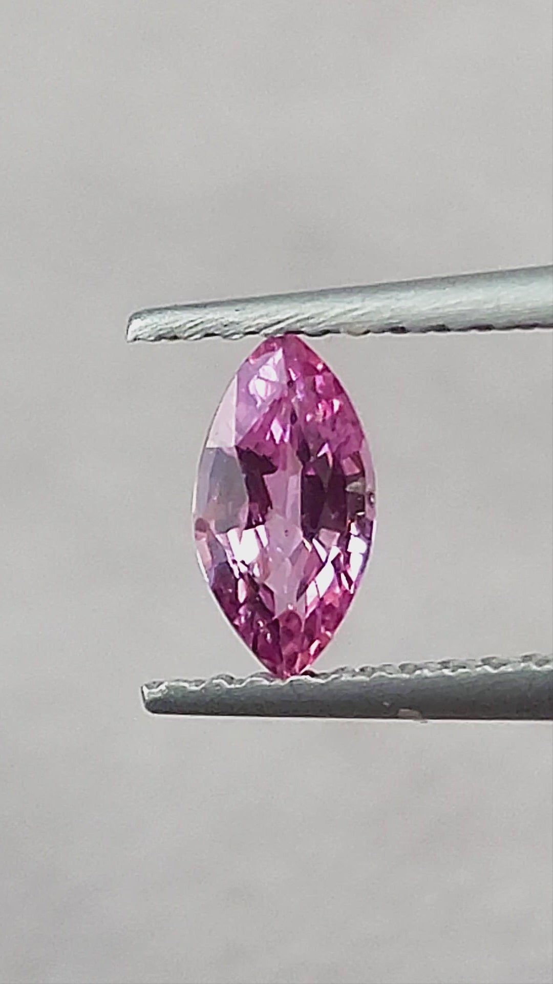 Pink marquise sapphire rotating in tweezers, shown between fingertips, on a cream pad, on a white pad and on a palm.