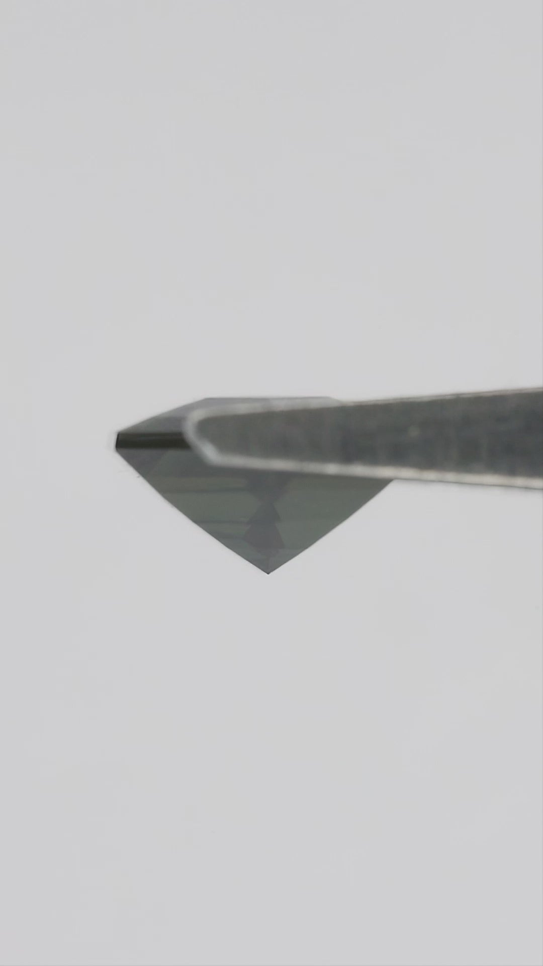 Natural-light video of the exact BNS205 sapphire tilting in tweezers and between fingers, showing changing reflections and scale.
