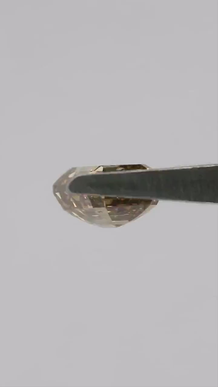 Natural-daylight tweezers video of the exact 1.01 ct natural fancy brownish-yellow emerald cut diamond rotating through face-up, tilted and profile views, then shown on a fingertip for scale.