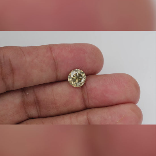 4K hand-scale video of the exact KL445 round brilliant diamond between fingers, showing its real-world size, pale champagne flashes and olive-gray reflections as it moves.