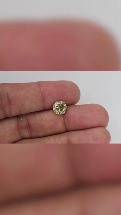 4K hand-scale video of the exact KL445 round brilliant diamond between fingers, showing its real-world size, pale champagne flashes and olive-gray reflections as it moves.