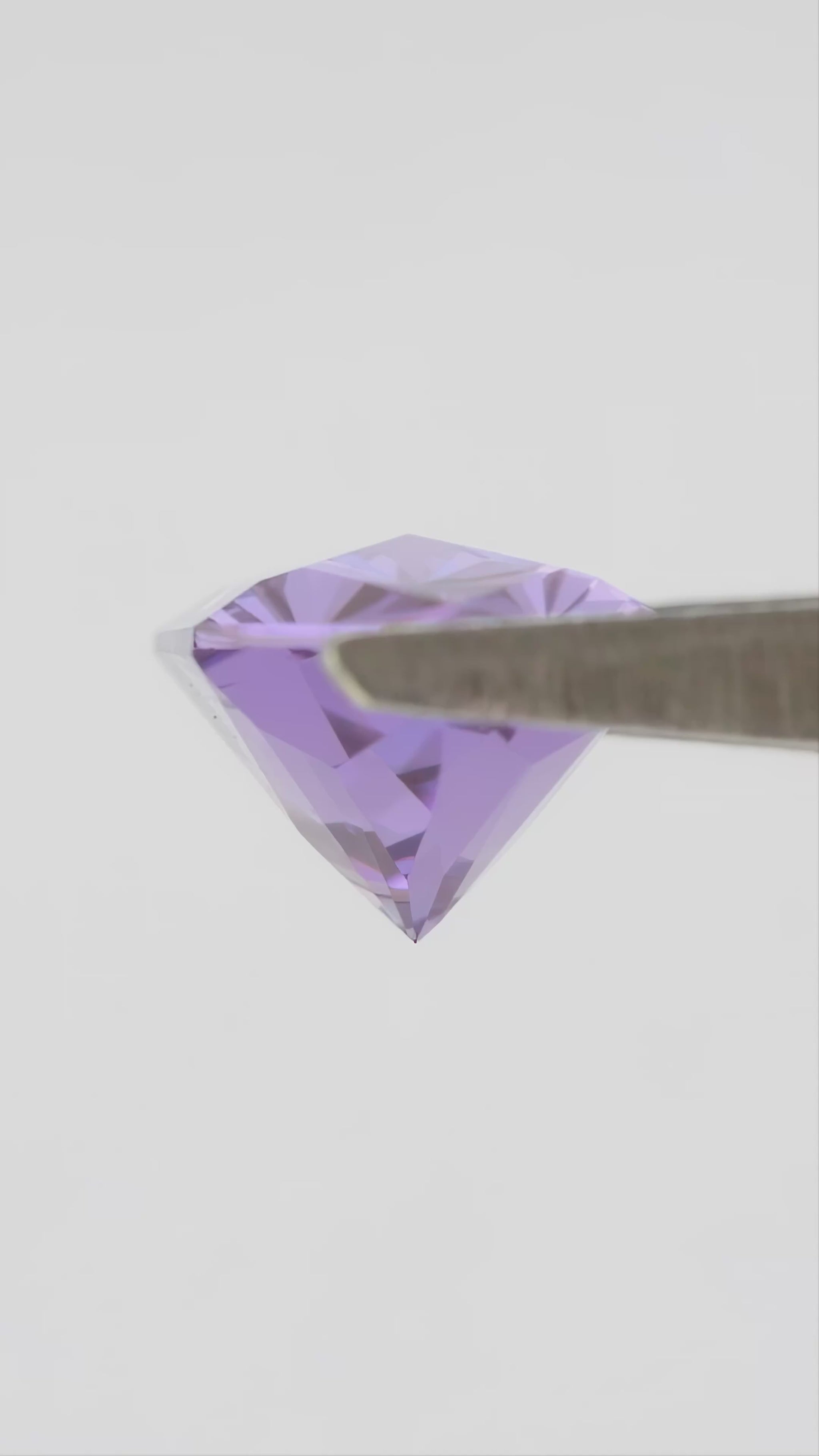Representative violet lab-grown sapphire rotating in tweezers, with face-up and finger-scale views.