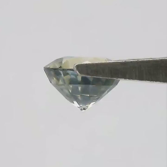Exact 1.48 ct natural parti sapphire moving in natural daylight, showing its round step cut and blended bluish green and yellow color.