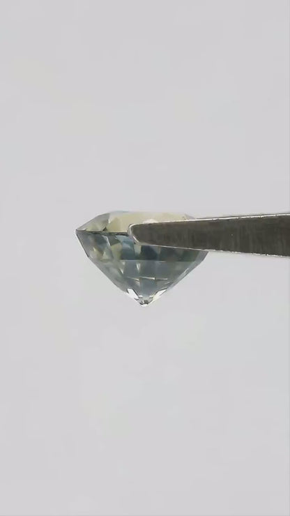 Exact 1.48 ct natural parti sapphire moving in natural daylight, showing its round step cut and blended bluish green and yellow color.