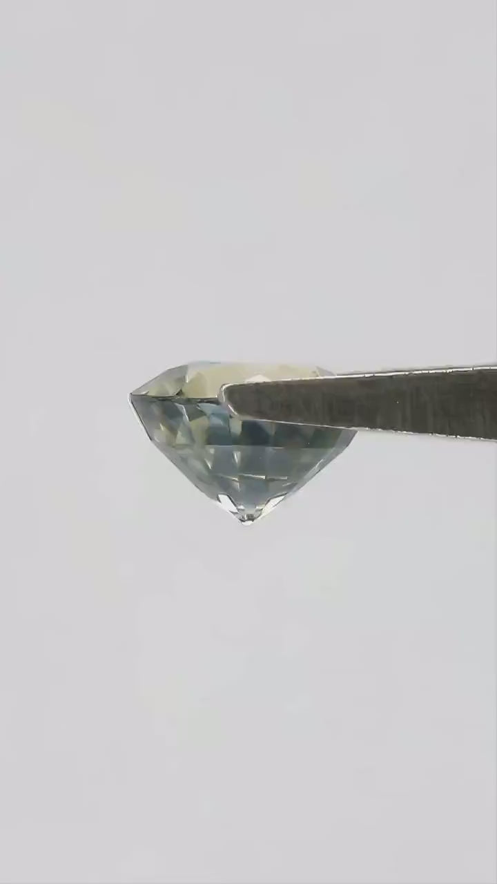 Exact 1.48 ct natural parti sapphire moving in natural daylight, showing its round step cut and blended bluish green and yellow color.