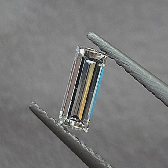 Video of a rectangular baguette diamond in tweezers at different inclinations, followed by fingertip scale views showing its long parallel facet reflections.