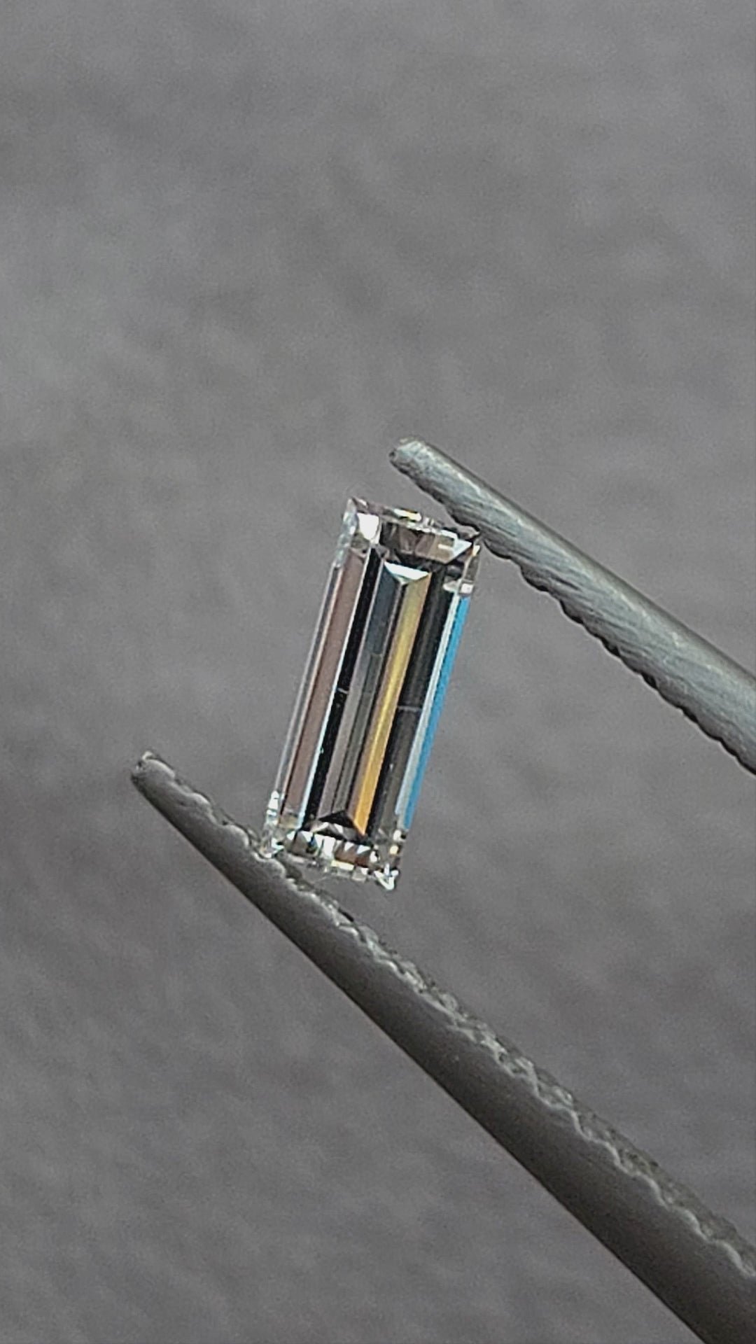 Video of a rectangular baguette diamond in tweezers at different inclinations, followed by fingertip scale views showing its long parallel facet reflections.