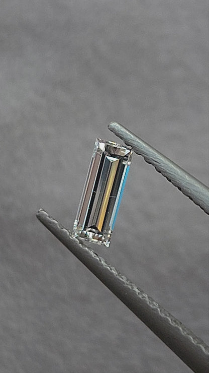 Video of a rectangular baguette diamond in tweezers at different inclinations, followed by fingertip scale views showing its long parallel facet reflections.