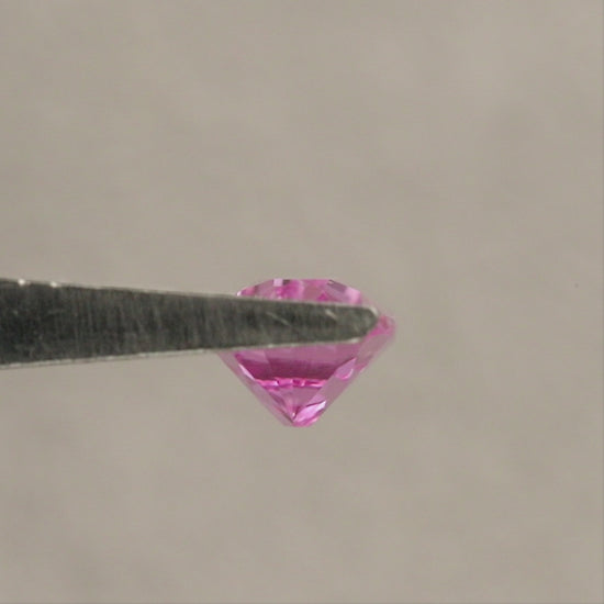 Representative pink lab-grown moval sapphire rotating in tweezers through face-up, tilted and profile views, followed by face-up fingertip views for scale.
