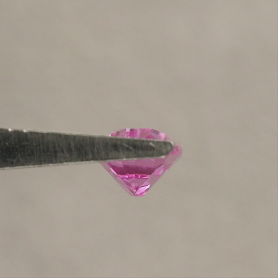 Representative pink lab-grown moval sapphire rotating in tweezers through face-up, tilted and profile views, followed by face-up fingertip views for scale.