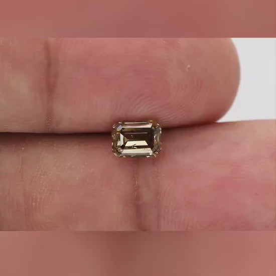 Natural-daylight fingertip video of the exact 1.01 ct natural fancy brownish-yellow emerald cut diamond showing scale, face-up color and step-facet reflections as it moves.