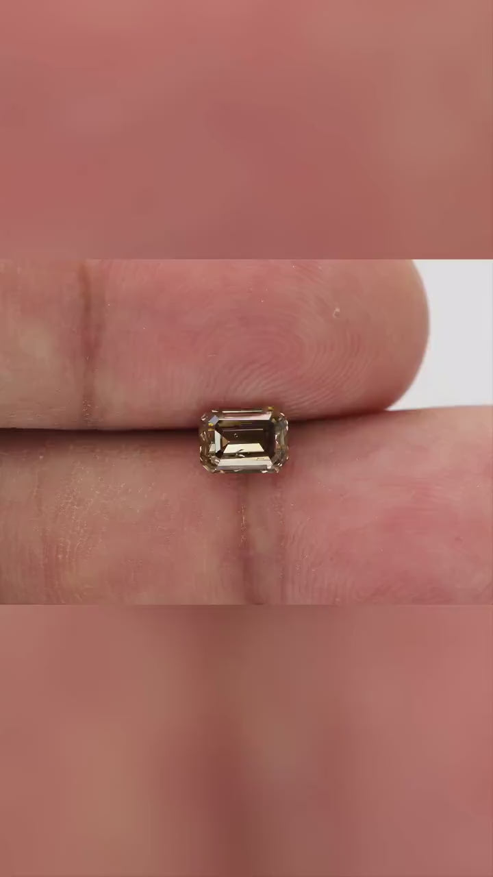 Natural-daylight fingertip video of the exact 1.01 ct natural fancy brownish-yellow emerald cut diamond showing scale, face-up color and step-facet reflections as it moves.