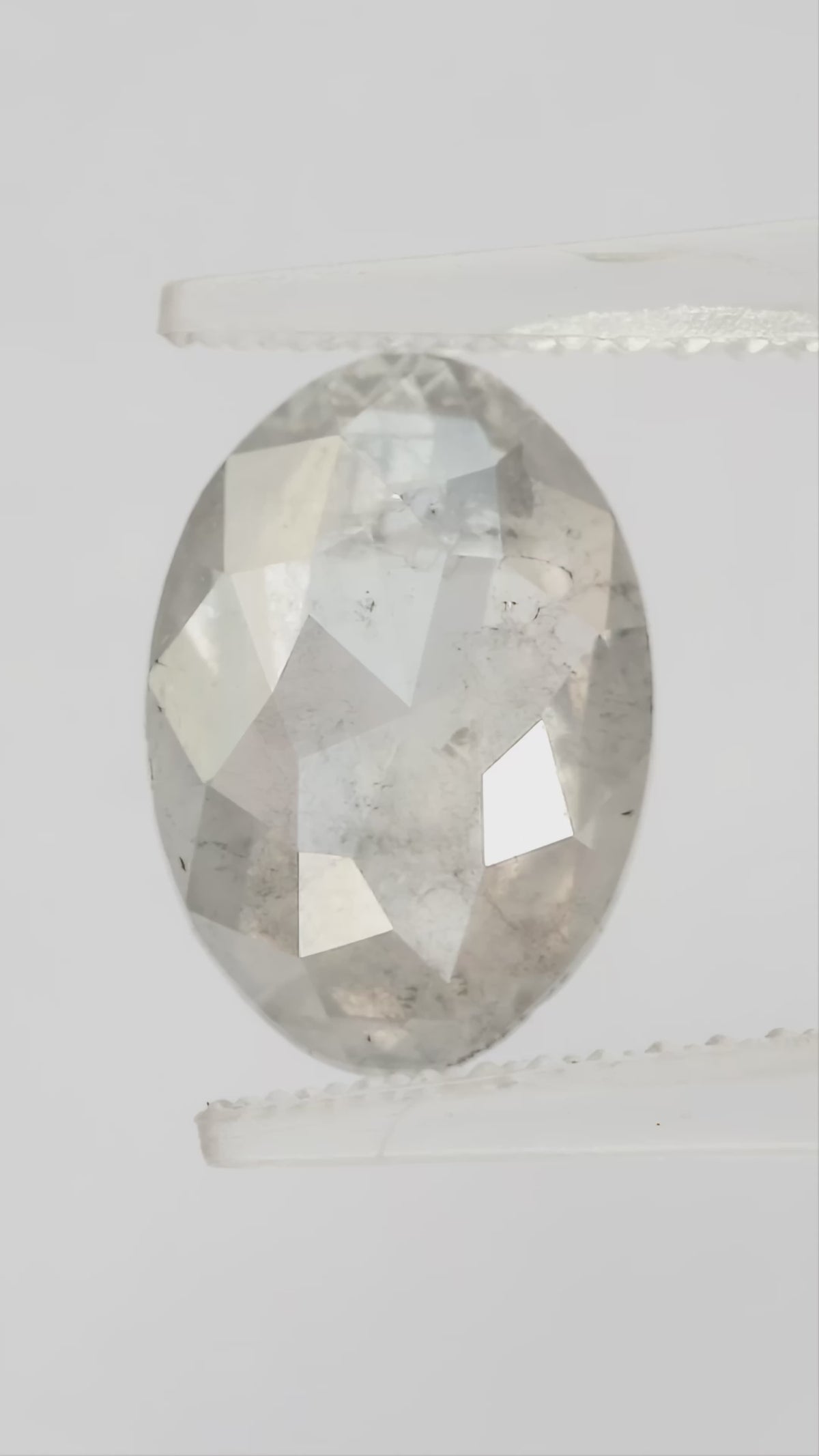 Finished video of the oval diamond rotating in pale tweezers, showing crown reflections in natural light.