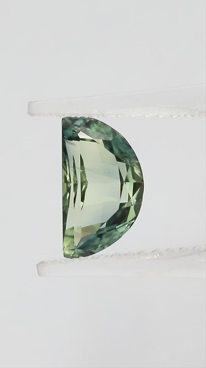 Video views of the half-moon parti sapphire in tweezers and on fingertips for scale, including its face-up appearance and checkerboard pavilion, with blue-green and pale yellow-green tones.