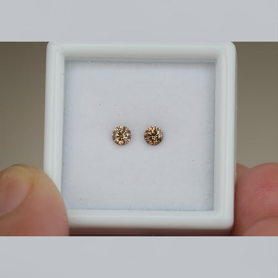 Video of the cognac brown diamond pair in a held white display box, with close face-up views and relative-scale context.